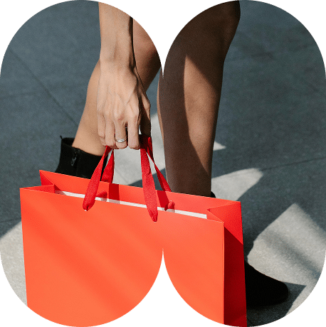 Persona sujetando una bolsa de papel roja con asas de cinta, en un entorno urbano.