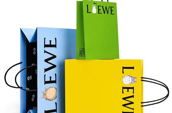 Bolsas de papel de lujo LOEWE en azul, verde y amarillo, con asas negras y detalles ilustrados, sobre fondo blanco.