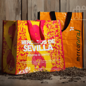 Dos bolsas reutilizables de Mercadona con diseño colorido apoyadas sobre una superficie de madera